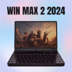 A thumbnail image for a video review of the WIN MAX 2 2024 mini-laptop. The black device is open in laptop mode, centered against a blurred background with a pink, blue, and white gradient. The screen displays a scene from a futuristic video game featuring four armed characters standing on a rocky terrain with flying ships in the background. The full QWERTY keyboard is visible. Large, bold, black text reading "WIN MAX 2 2024" is overlaid across the top of the image.