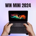 A thumbnail image for a video review of the WIN MINI 2024 handheld gaming laptop. The black, clamshell device is held open by two hands against a blurred purple and white background. The screen displays a colorful, abstract wallpaper with red, green, and blue flowing light trails. The device's integrated gaming controls (D-pad, analog sticks, face buttons) and full QWERTY keyboard are visible below the screen. Large, bold, black text reading "WIN MINI 2024" is overlaid across the top of the image.