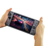 A pair of hands holding the GPD WIN 5 handheld gaming console, isolated against a white background. The console is dark grey and its large widescreen display shows a high-speed racing game with a futuristic car speeding through a city at night, with motion blur effects. The ergonomic grips and all control buttons are visible.