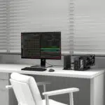 Configurazione della scrivania con un monitor widescreen che visualizza codice e finestre del terminale, un PC compatto e una GPU esterna sulla destra, una sedia bianca e tende sullo sfondo.