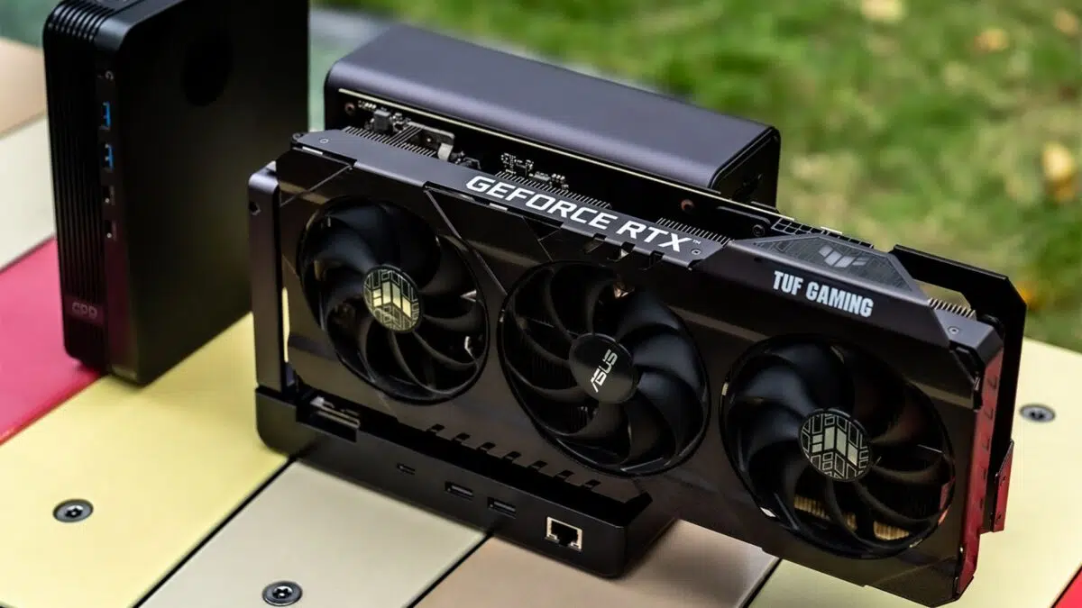 Графична карта GeForce RTX с три охлаждащи вентилатора и брандинг "TUF GAMING", инсталирана в компактна компютърна кутия върху плот на открито.