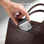 Close-up of a hand placing a silver multi-port charger into the side pocket of a brown leather handbag, with the text 'Multi-port Charging, Worry-free Travel' visible in the background.