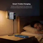 Chargeur intelligent mural à côté d'un lit, avec un téléphone en charge sur la table de nuit.