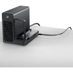 Black desktop NAS/enclosure with a pull-out drive bay and front hexagonal vent, power button, and a cable connected on a white desk surface.